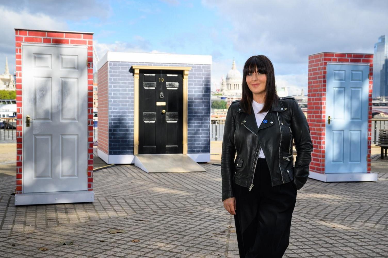 Ann Richardson wearing a leather jacket and black trousers stands in front of an art installation of doors at the Southbank Centre in central London