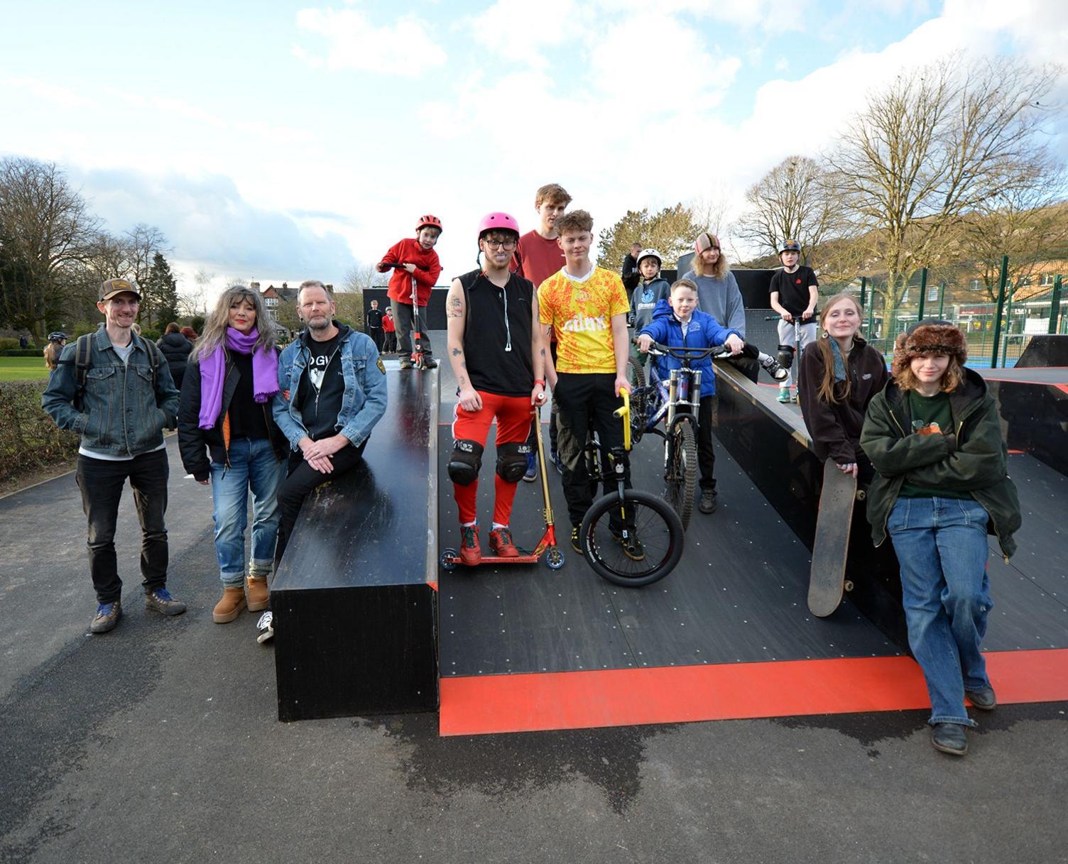 A group of people with skateboards, BMX bikes and scooters pose on the plaza ramp of the new skatepark.