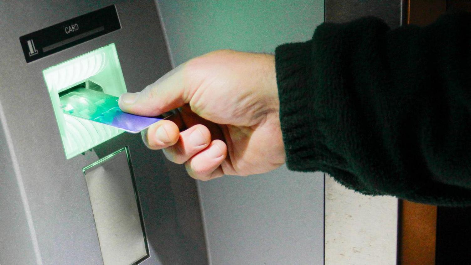 Close-up of a hand pushing a bank card into a cash machine