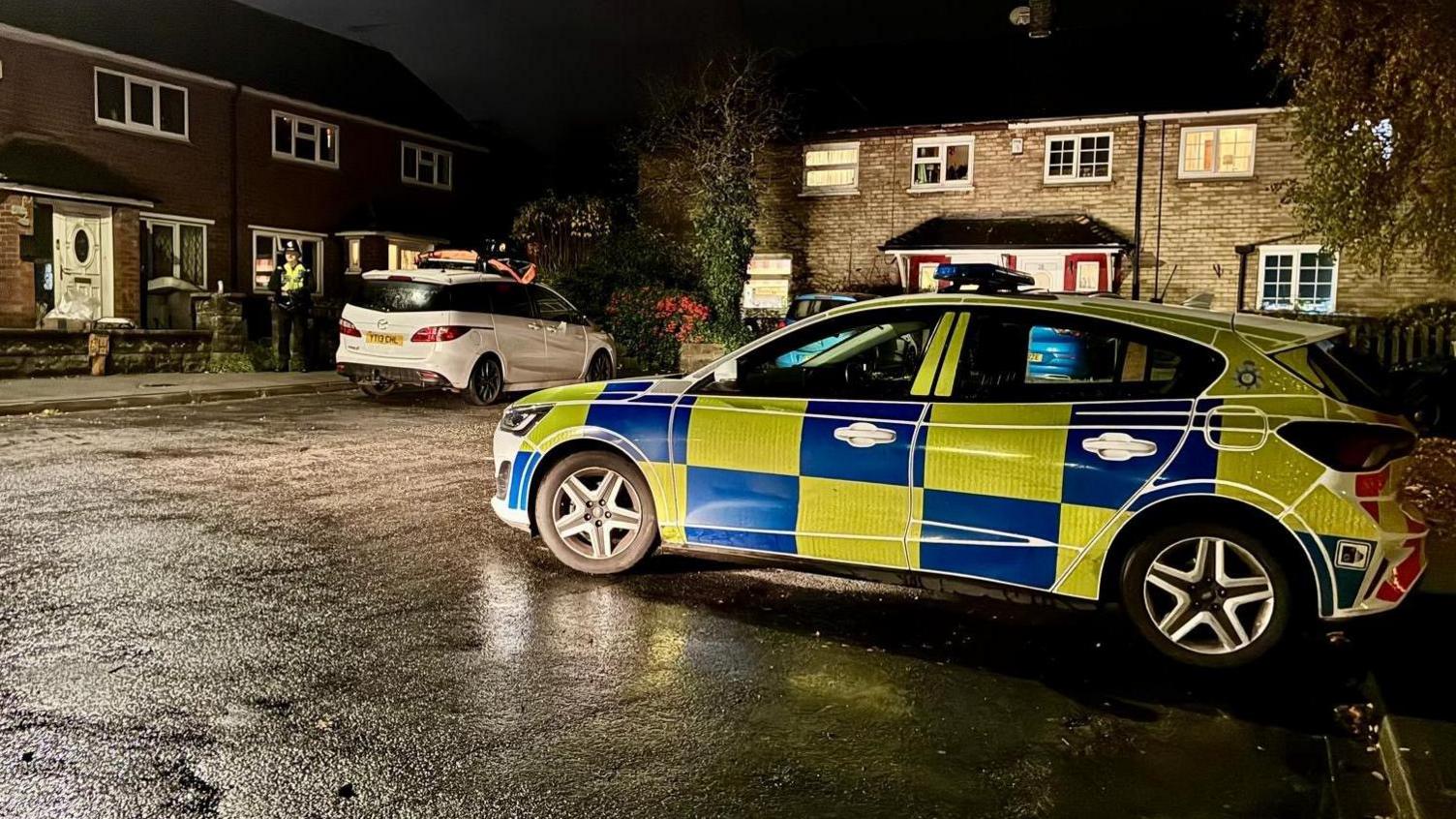 A police car is parked on a residential street on a wet night.