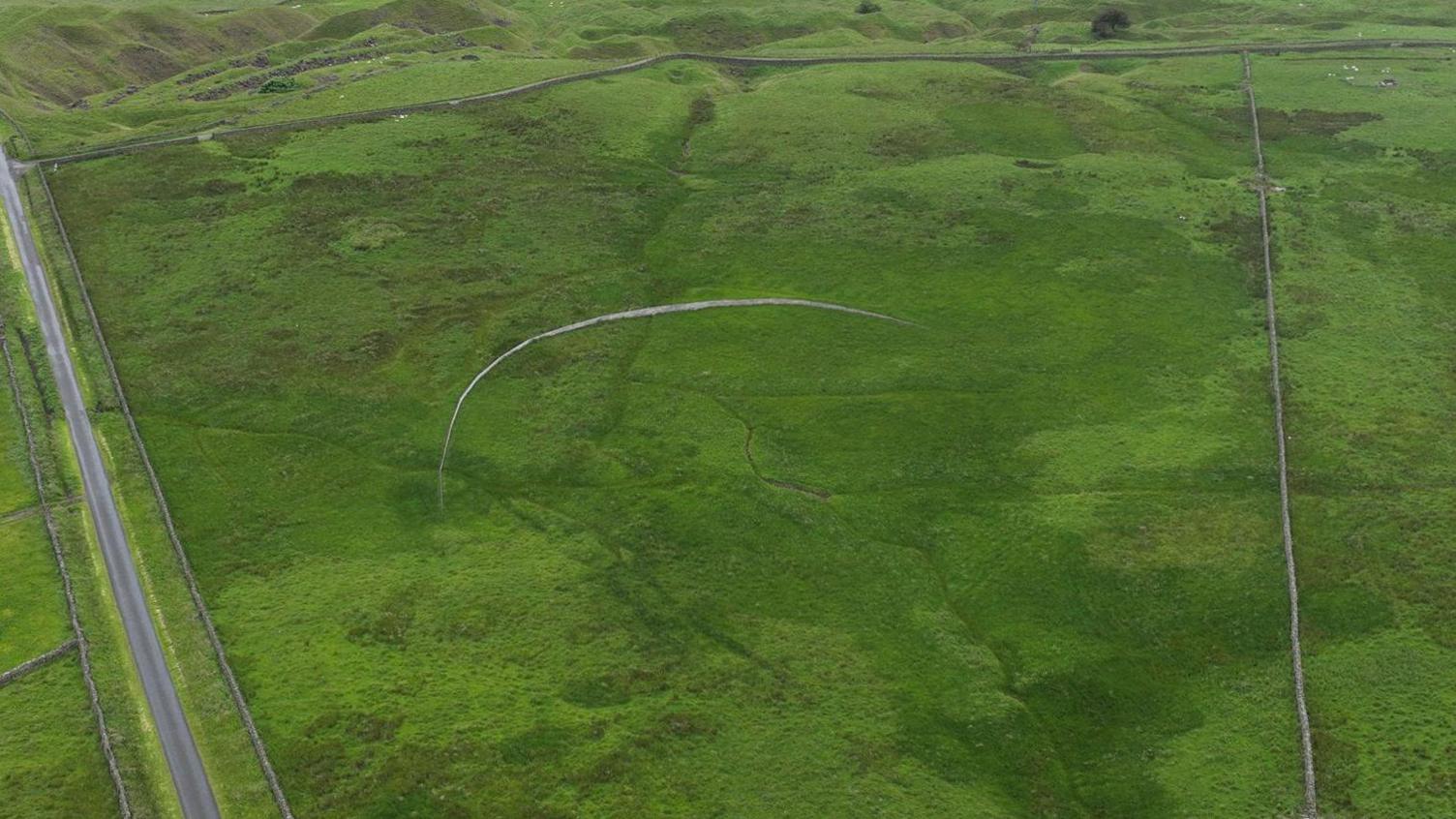 An aerial view of a timber fence which has been built in the middle of a field. The fence has been built in a crescent shape.