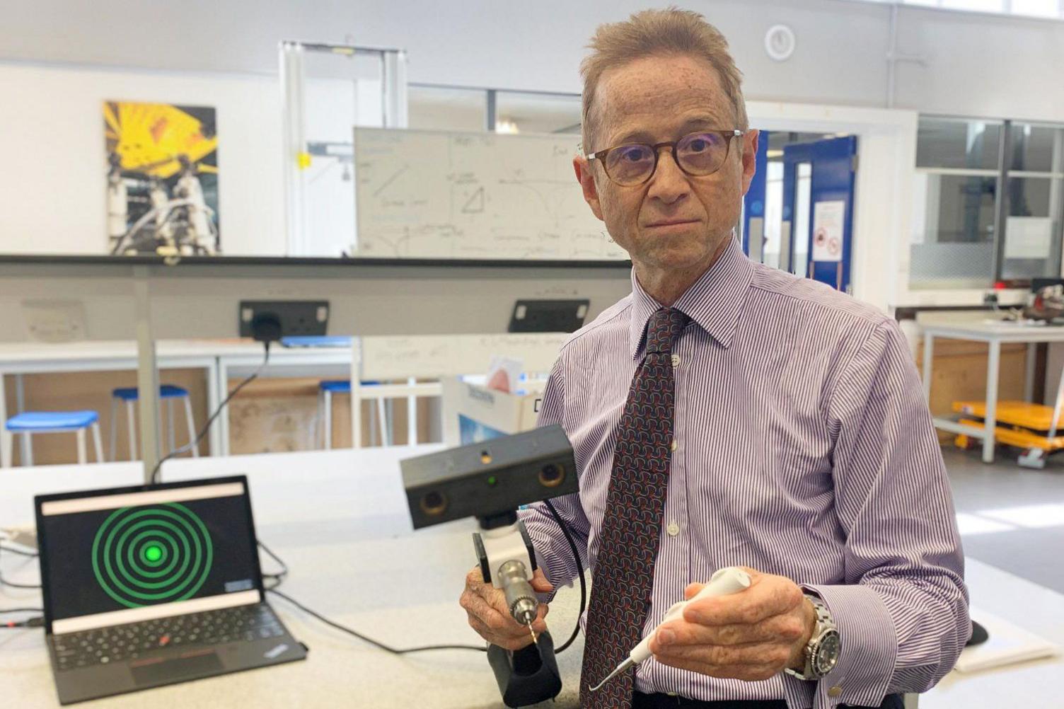 Professor Grey Giddins, Consultant Orthopaedic and Hand surgeon, holding a new medical device called a 'drill guidance system.'