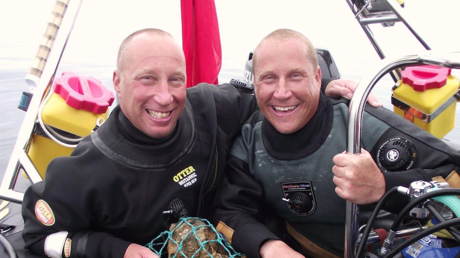 Julian Barnwell with his arm around his brother Lincoln both in diving equipment and sat on a boat