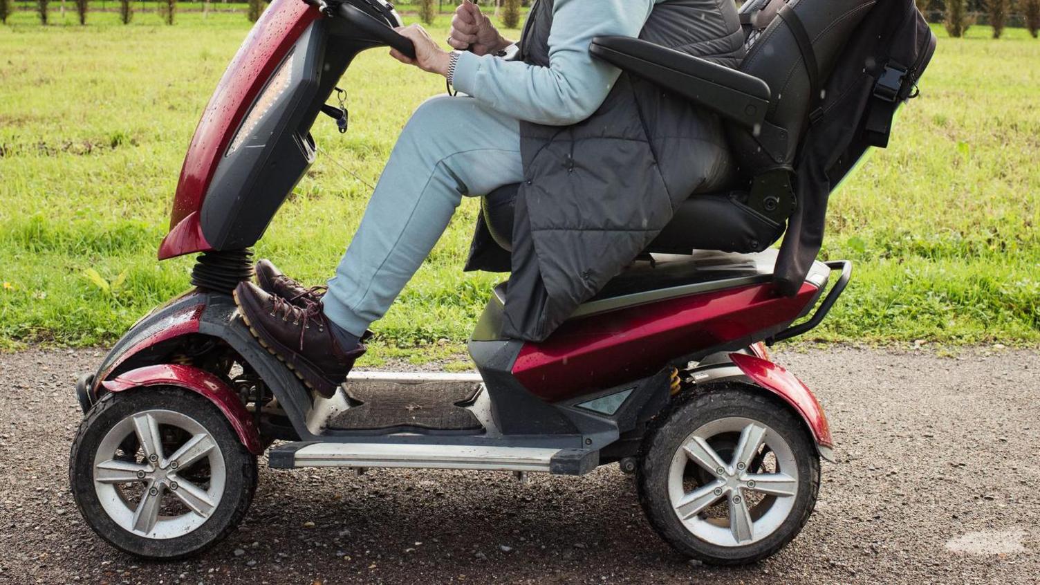 A stock photo of a woman on a powered mobility scooter outside in a park