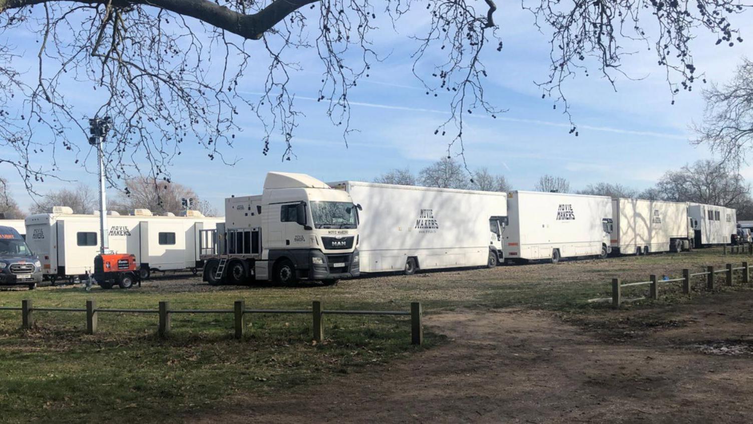 A series of white vehicles and trailers stationed on a park. 