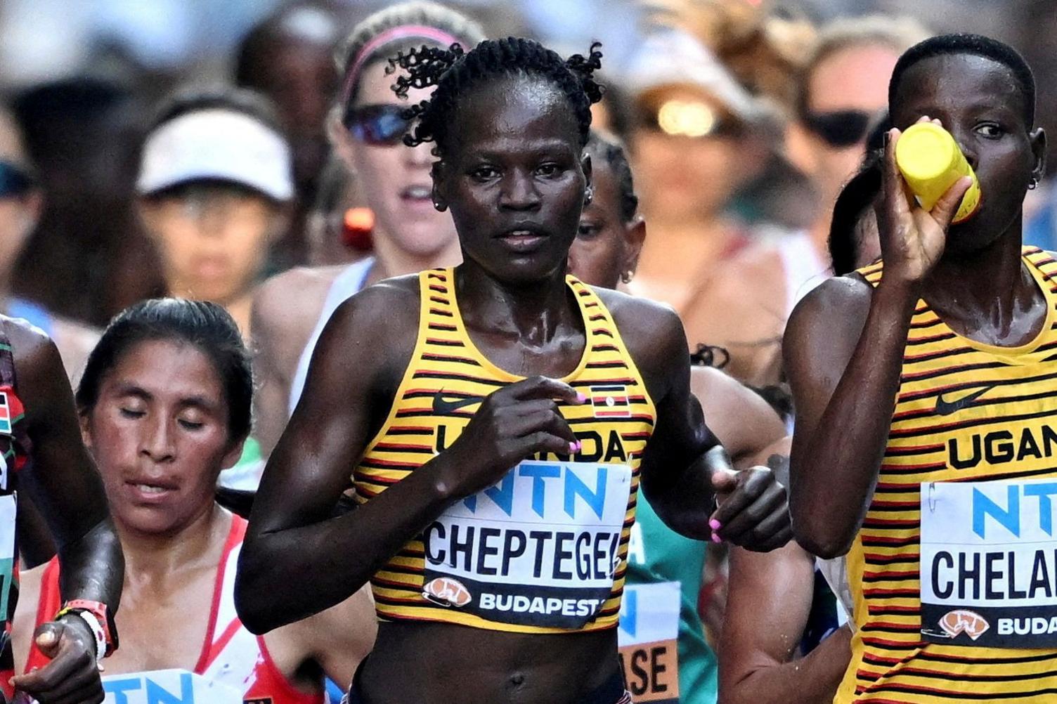 Runner Rebecca Cheptegei, in a striped yellow and black sports top, pictured with other runners