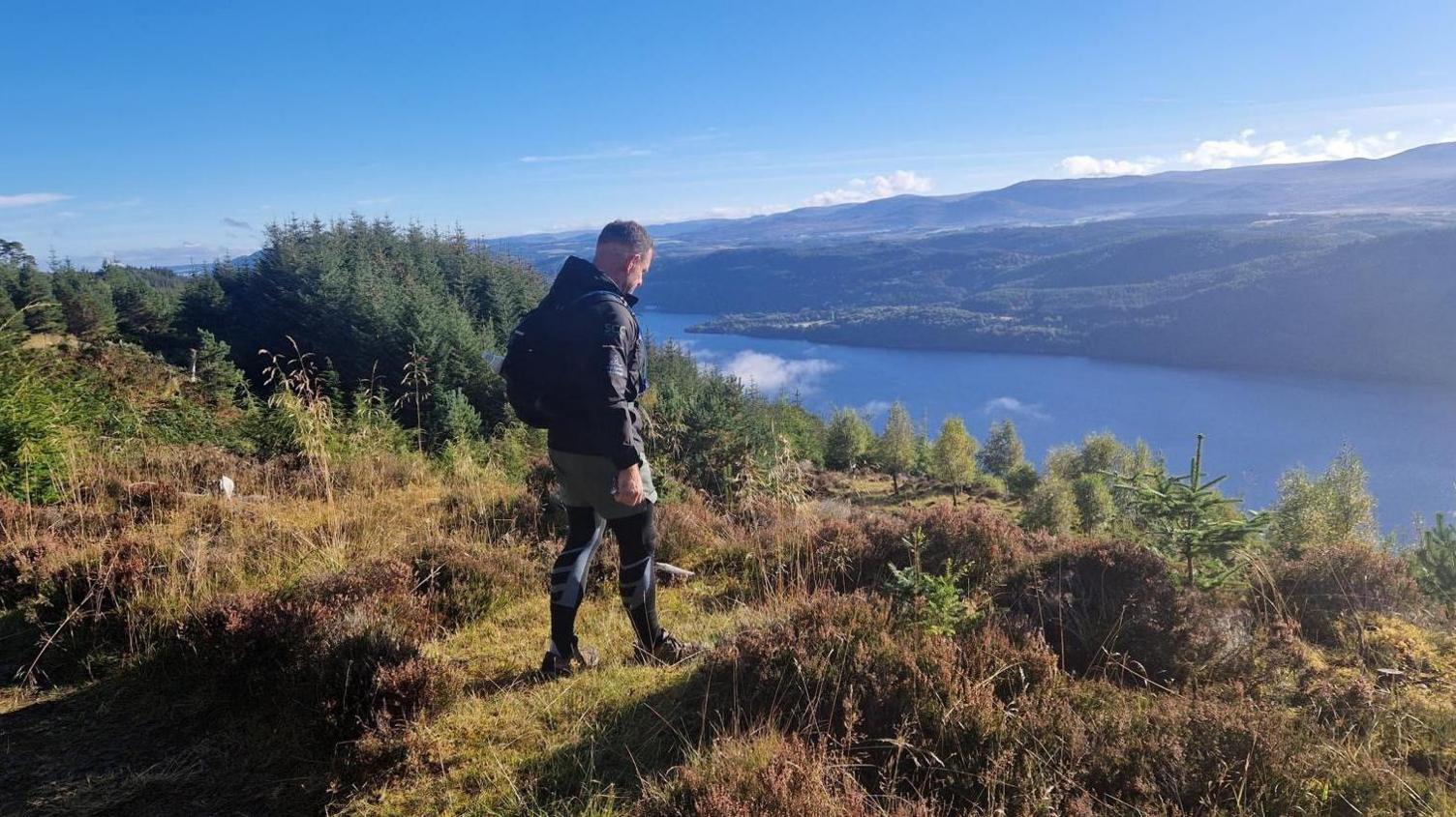 Andrew Jenkins on a grassy hill looking out over water and mountains