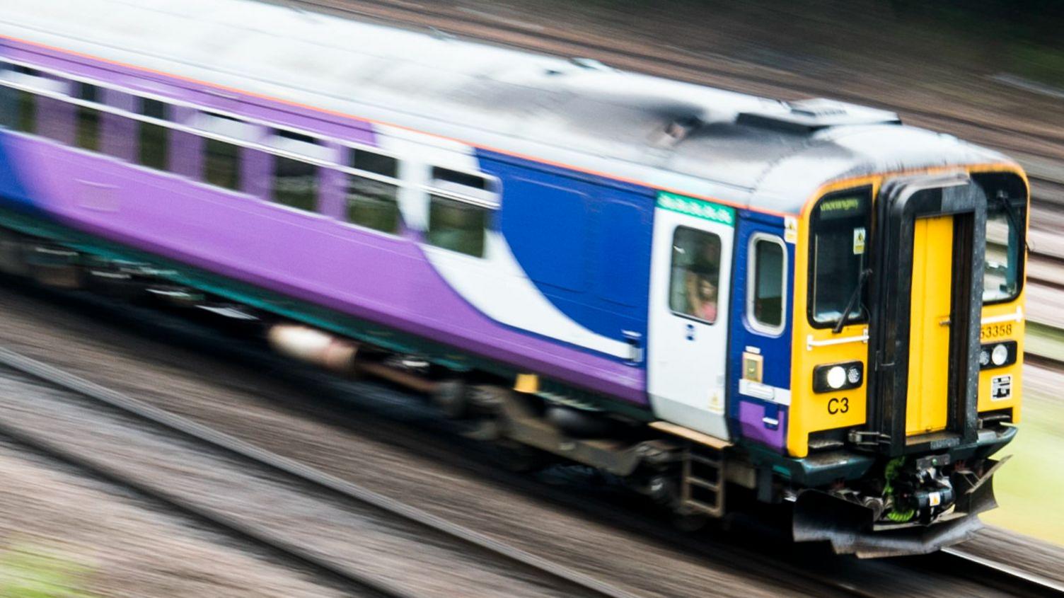 A train in purple and blue Northern Trains livery is pictured in motion on train tracks