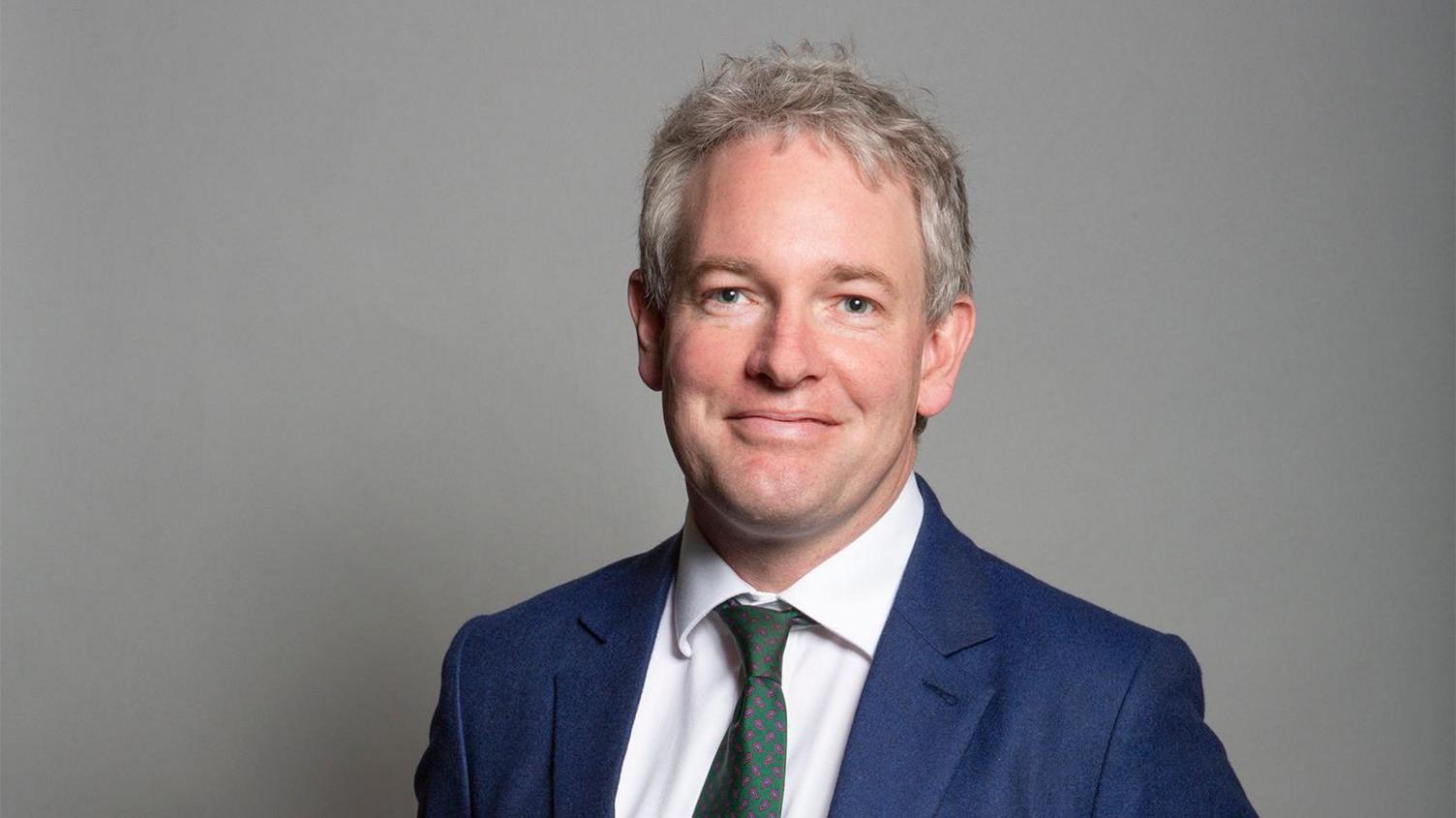 Danny Kruger wearing a blue suit with a green tie