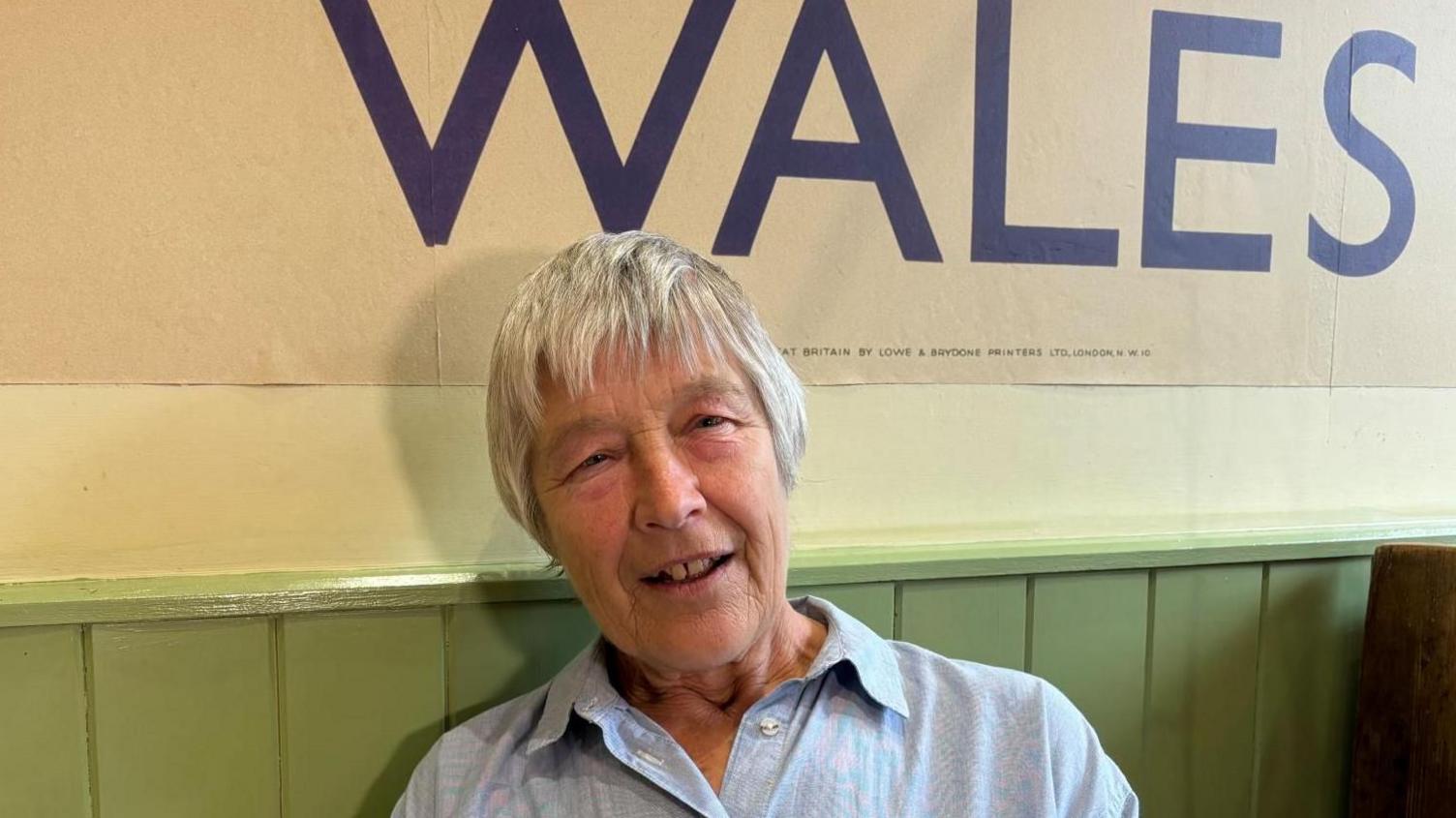 Hilary Dodd in a cafe with a Wales sign behind her on the wall