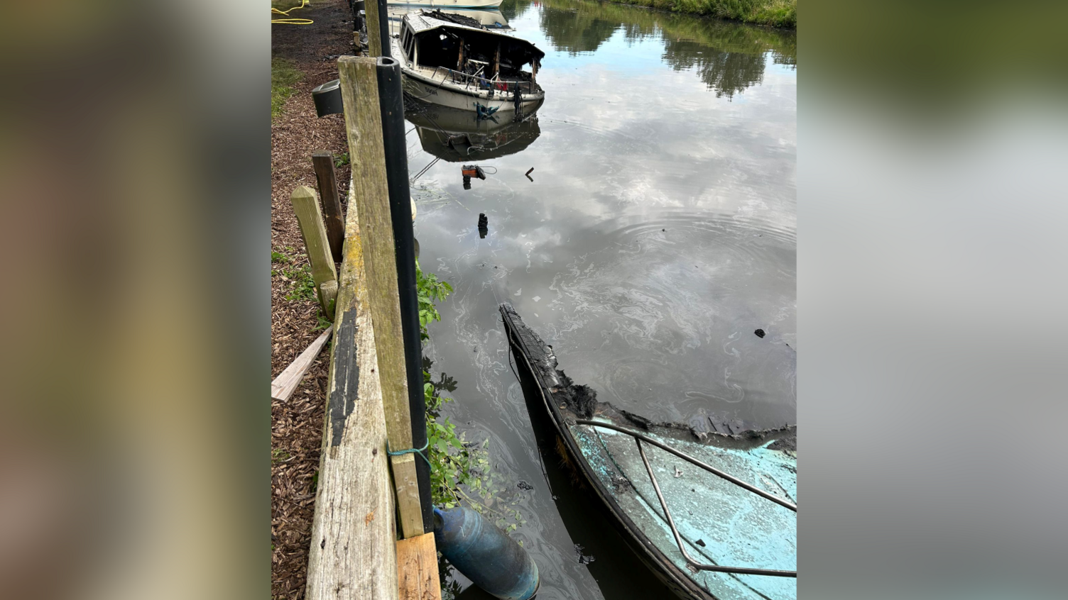 A partly sunken fire damaged boat with another fire damaged boat in the background