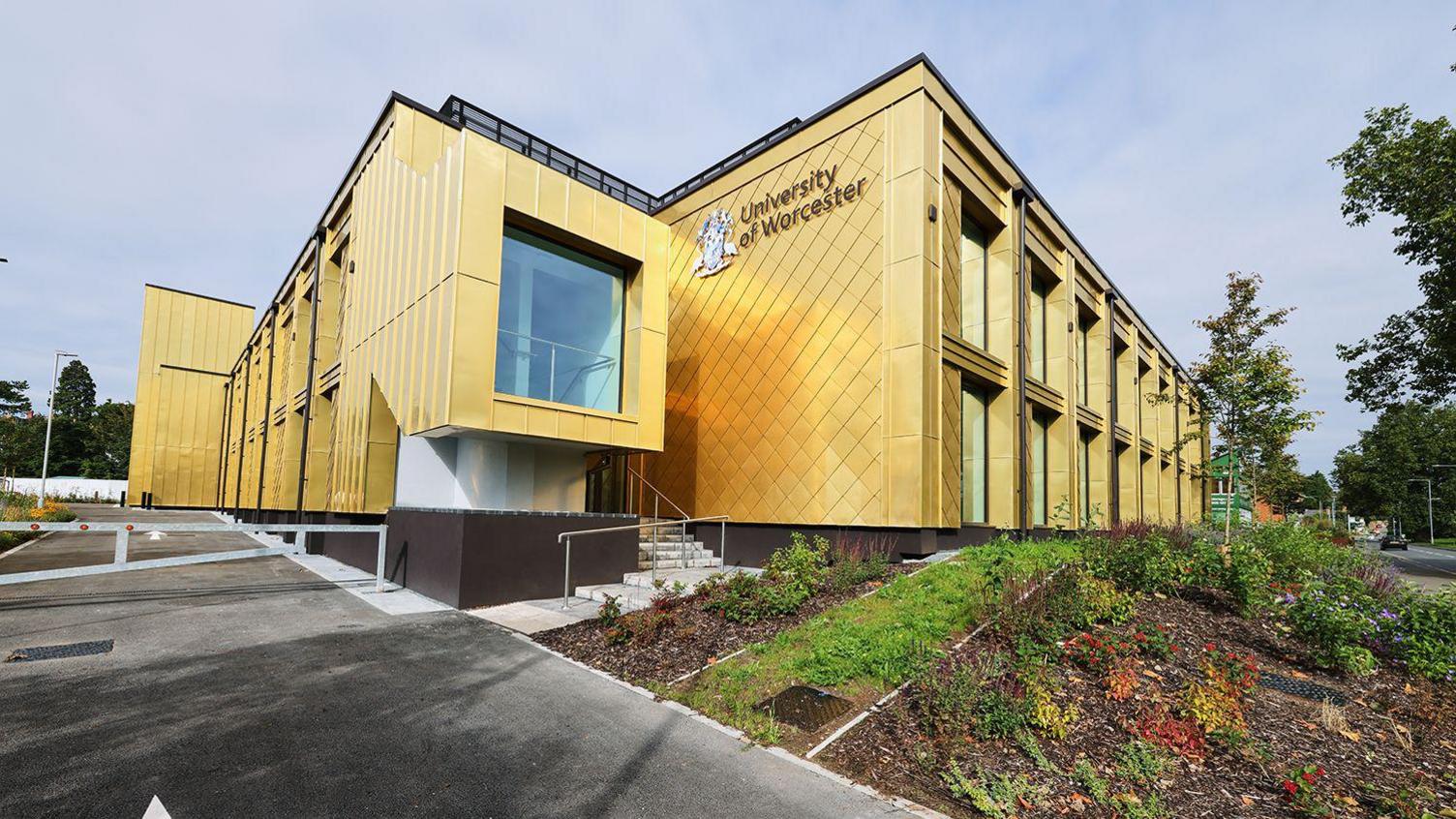 The University of Worcester's Three Counties Medical School. It is a yellow building with the university logo and crest on the side.