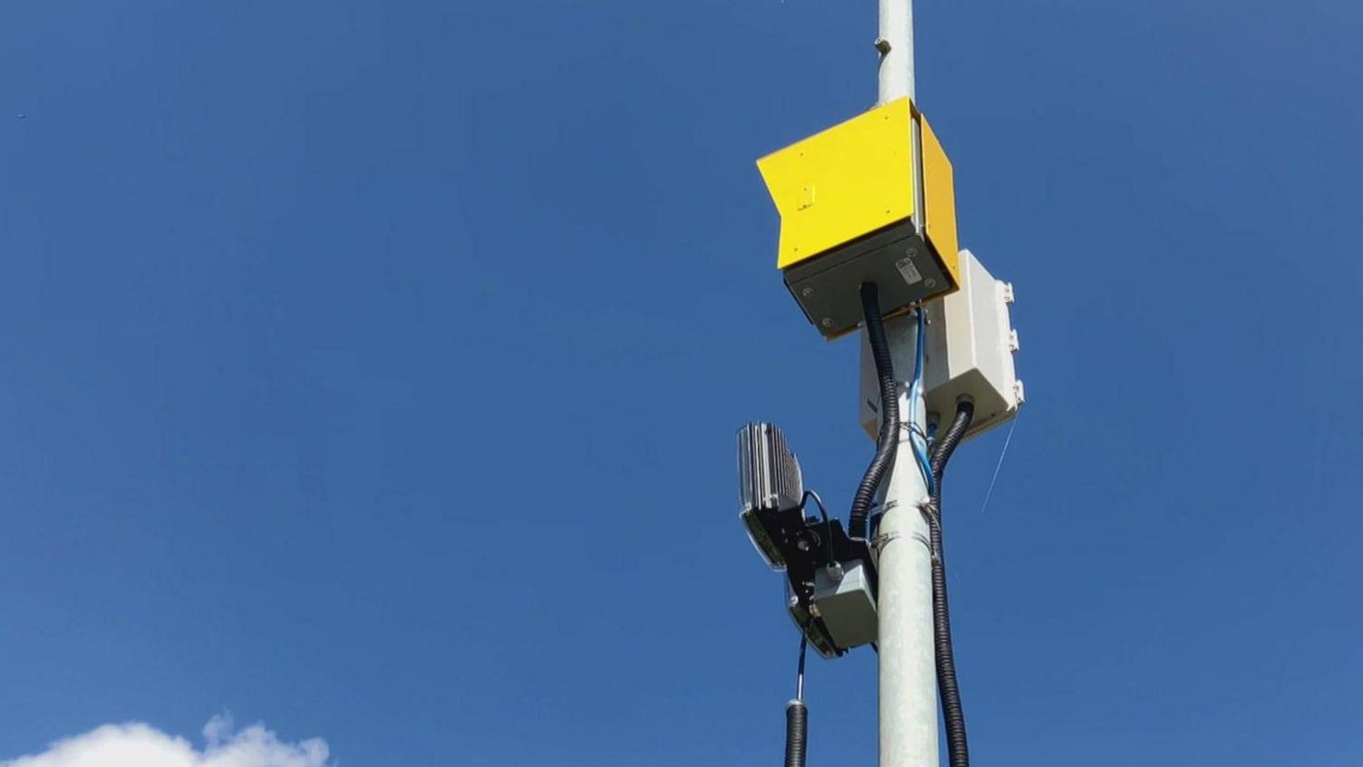 A yellow box with two sensors, attached to a lamppost.
