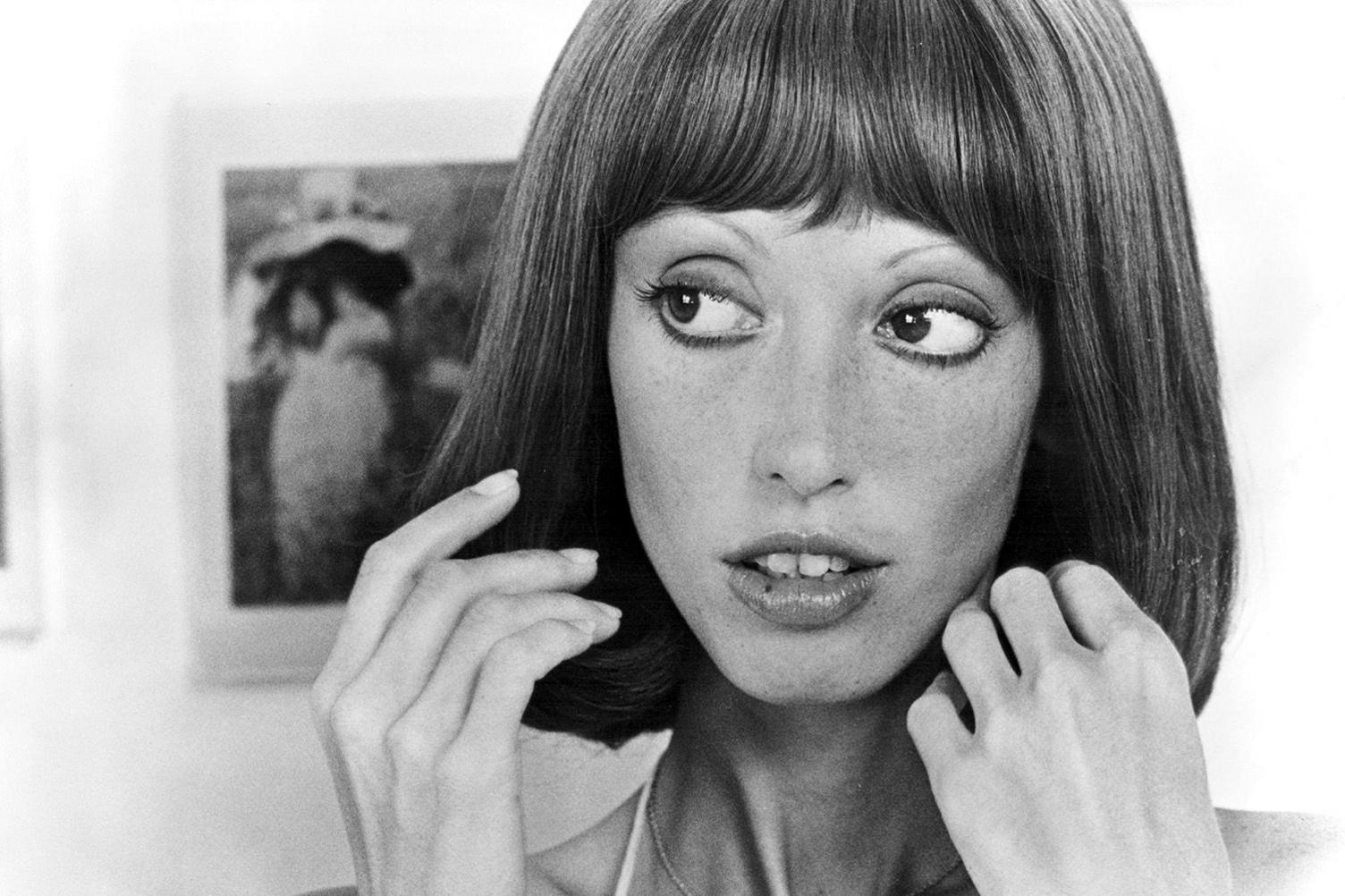 Black and white head shot of Shelley Duvall, taken from the 1977 film Three Women. She is looking away from the camera, wearing make-up and touching her hair, which is shoulder-length.