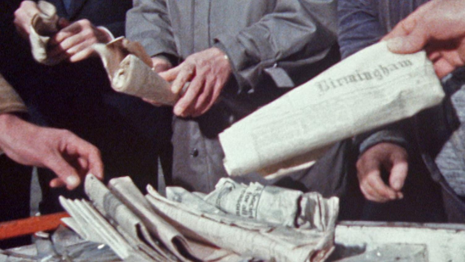 Close up of hands picking up old newspapers from Birmingham which were stored inside a time capsule.