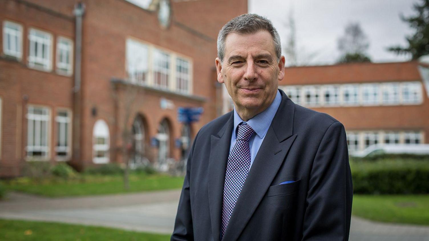 Prof David Green dressed in a suit, standing outside the University of Worcester's main building