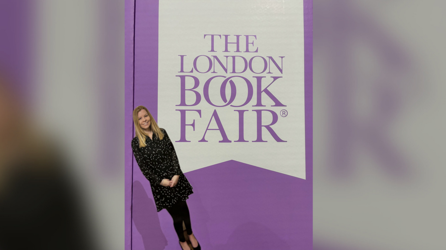 Chopstick Sally standing in front of a London Book Fair poster