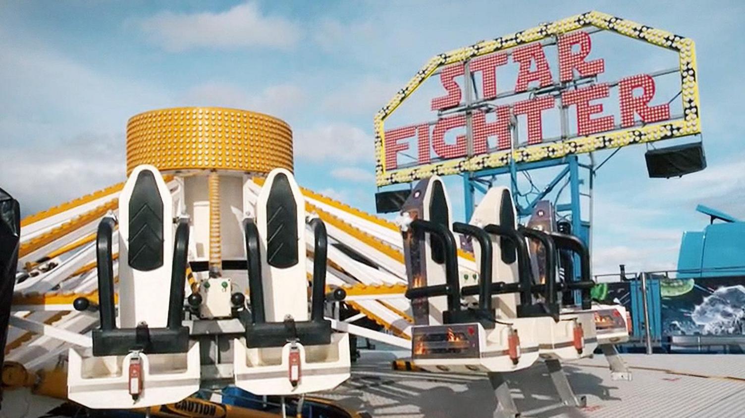 A white and gold funfair ride under a blue sky with a Star Fighter sign behind