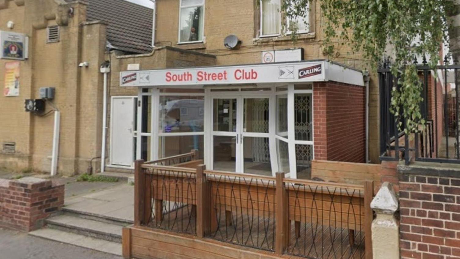 A former working men's club entrance, with three steps, wood and metal railings lead from the street.