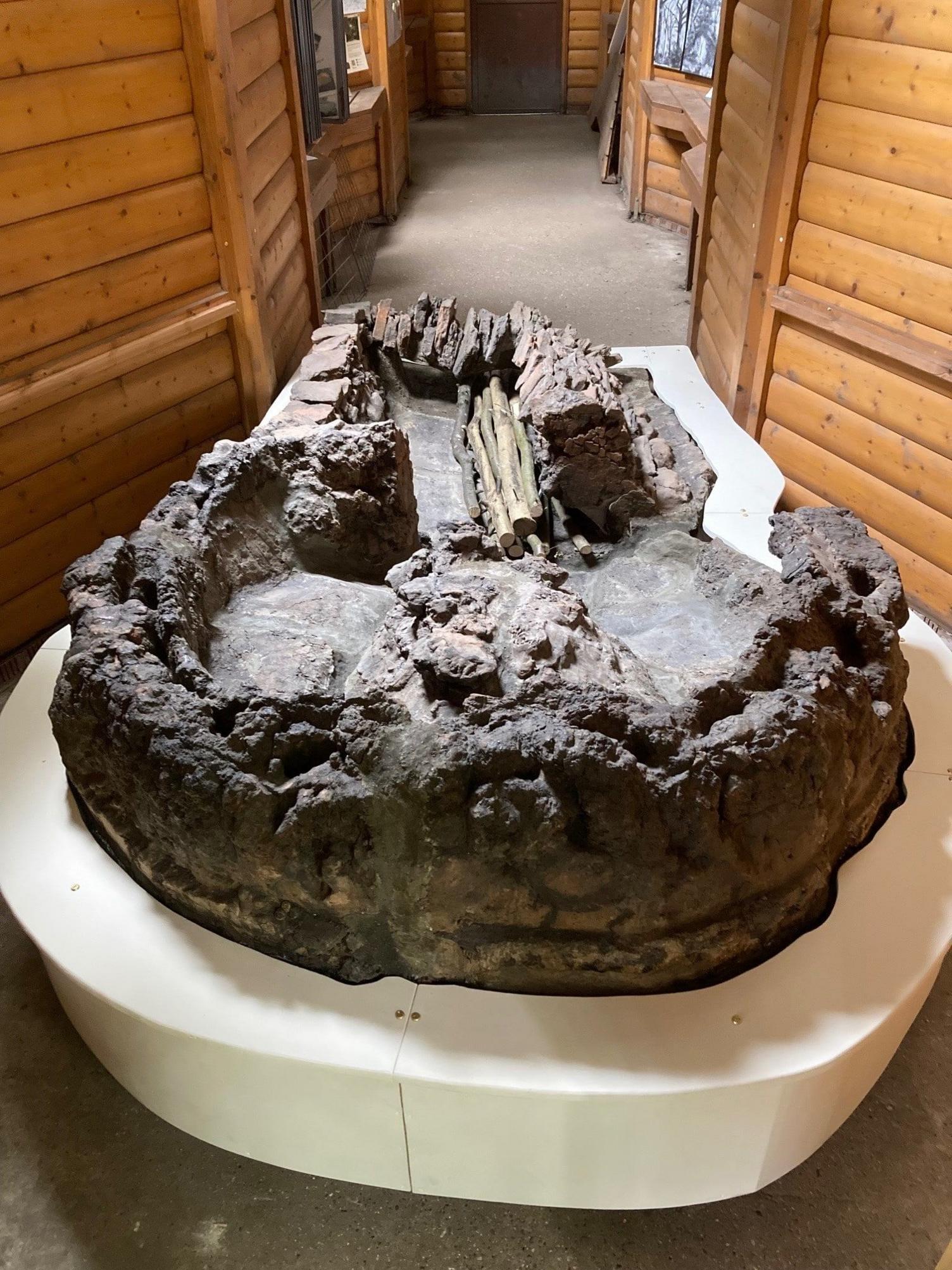 A full shot of the ancient Roman pottery kiln with eroded stone and brick walls, showing a weathered, sunken structure used for high-temperature firing, in the information centre where it is being displayed