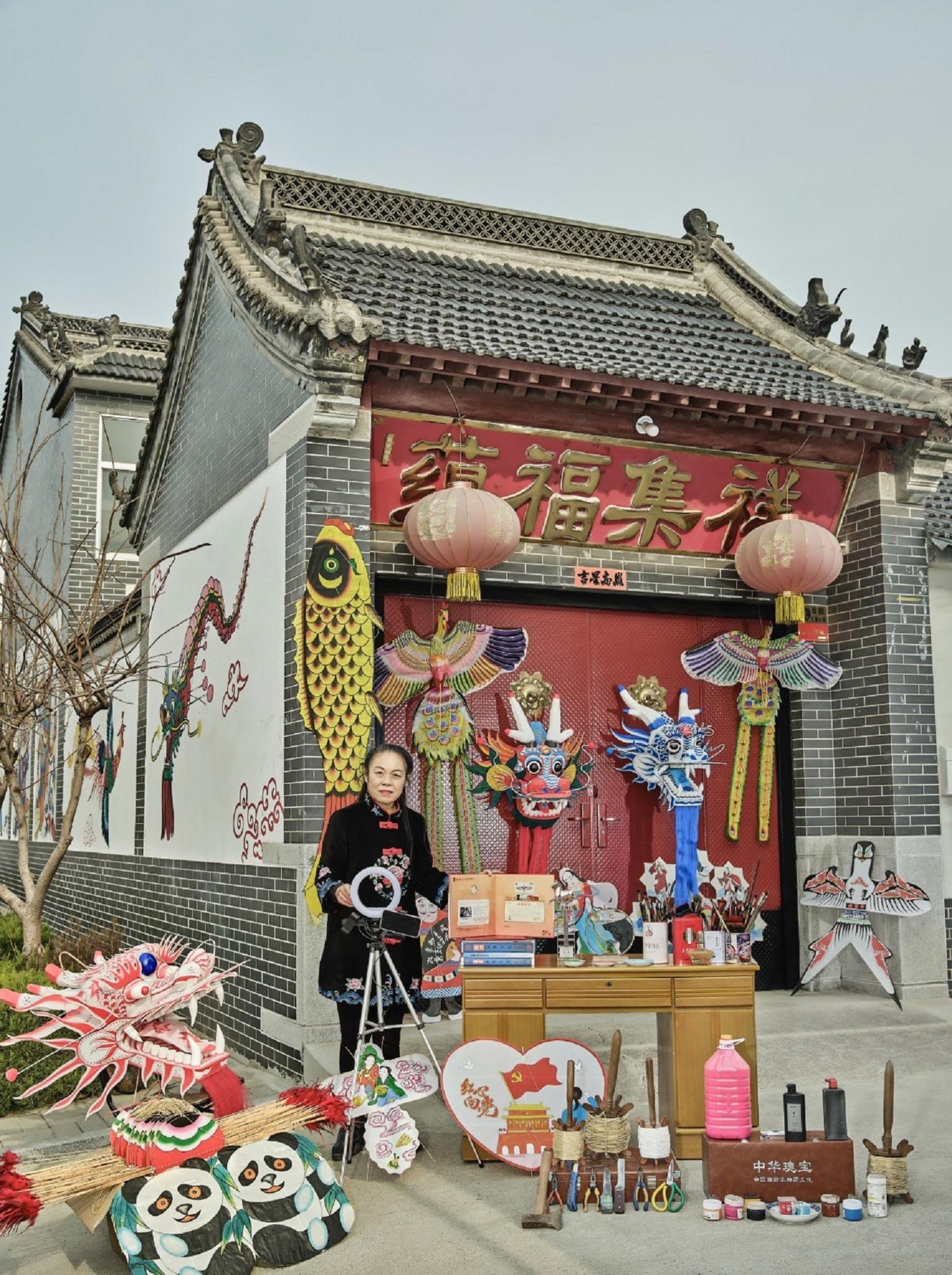 A woman stands in front of a wooden worktable surrounded an array of tools to create and design kites