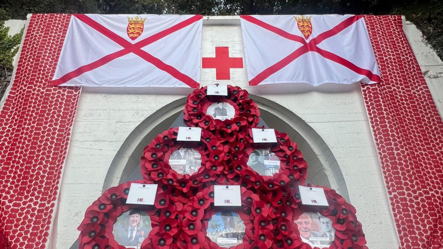 The front of the tunnel which is covered in poppies and two large Jersey flags. The tunnel entrance is covered by a large triangular wreath made up of poppies.