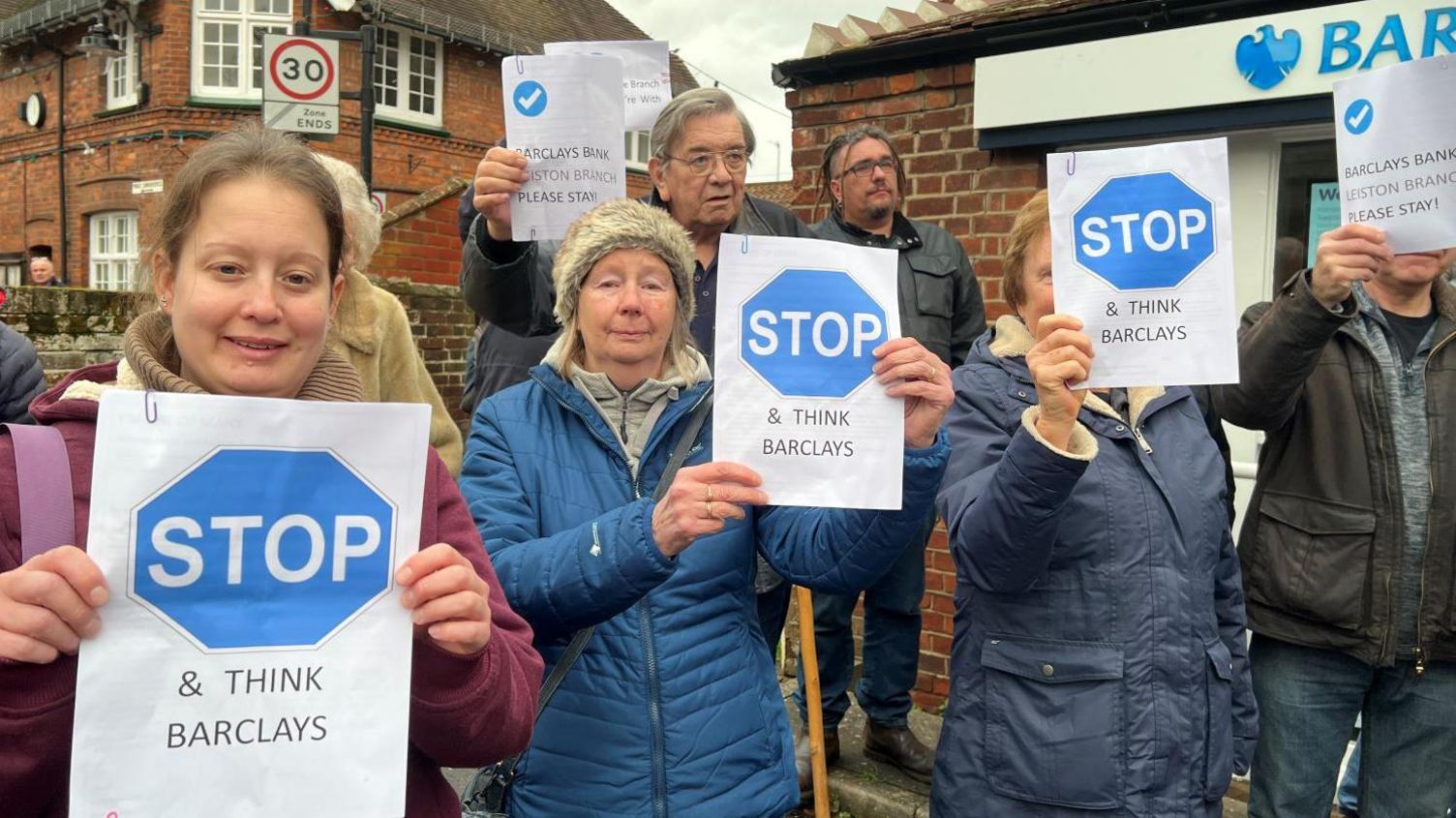 Protesters holding signs that say 'stop and think Barclays'