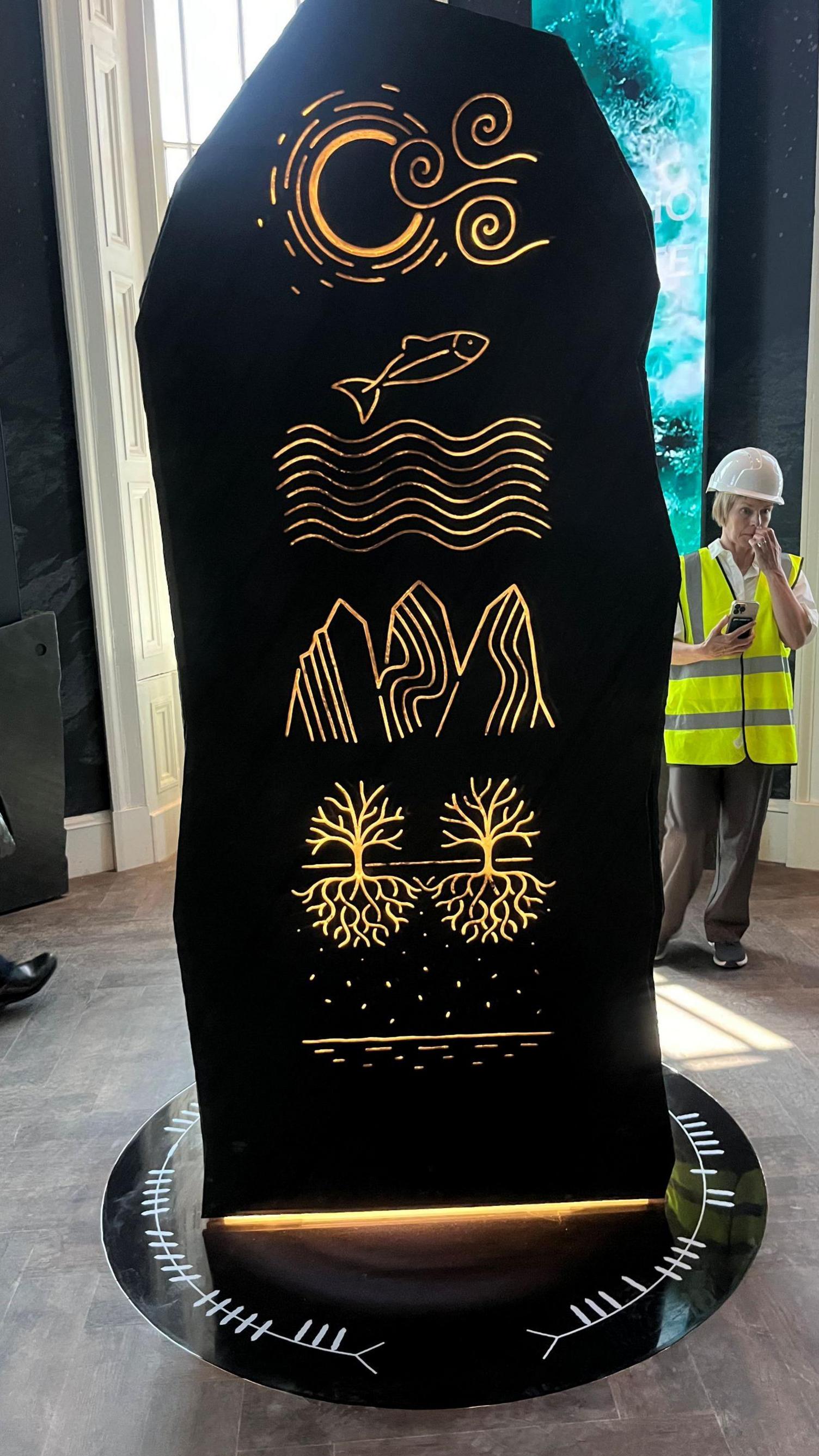 The "stone" is black and includes a number of symbols and drawings, including a fish and water, mountains and trees.