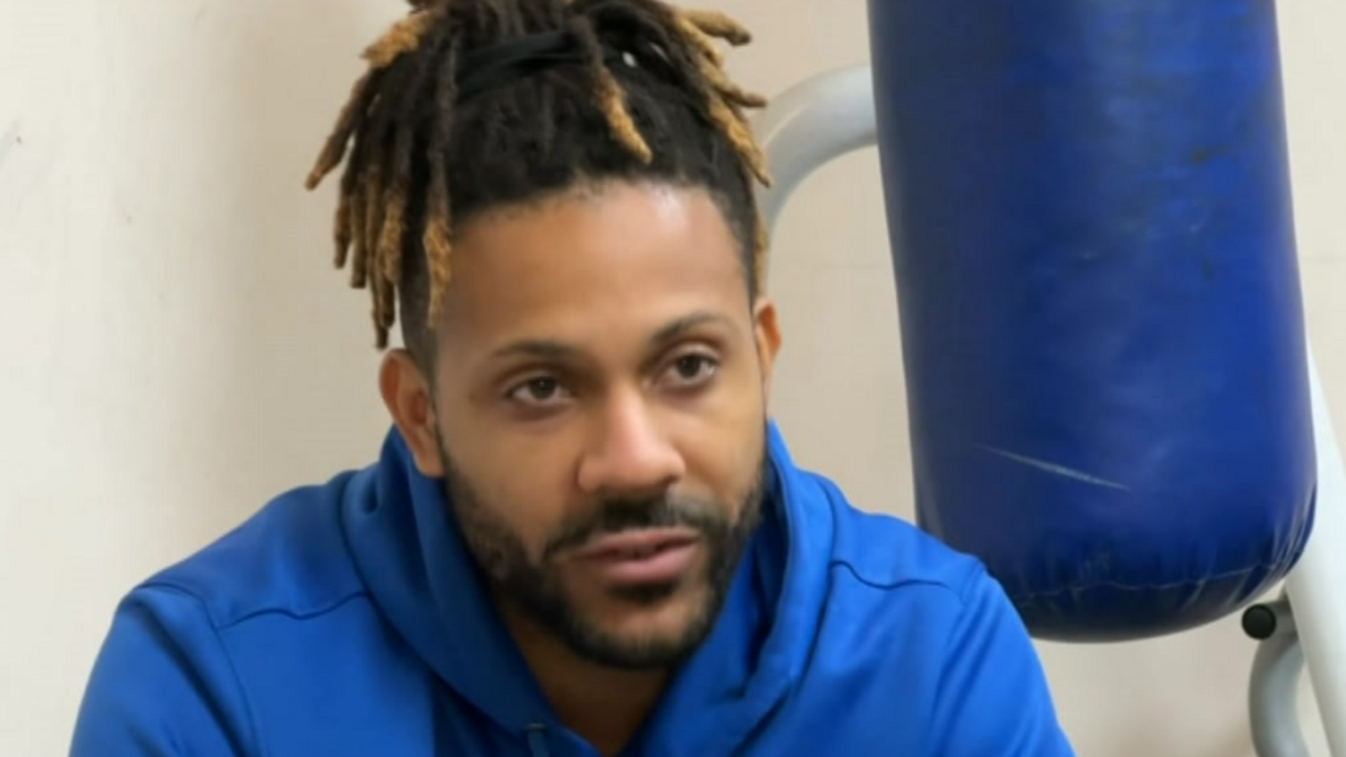 A black man with hair tied up, wearing a blue hoodie