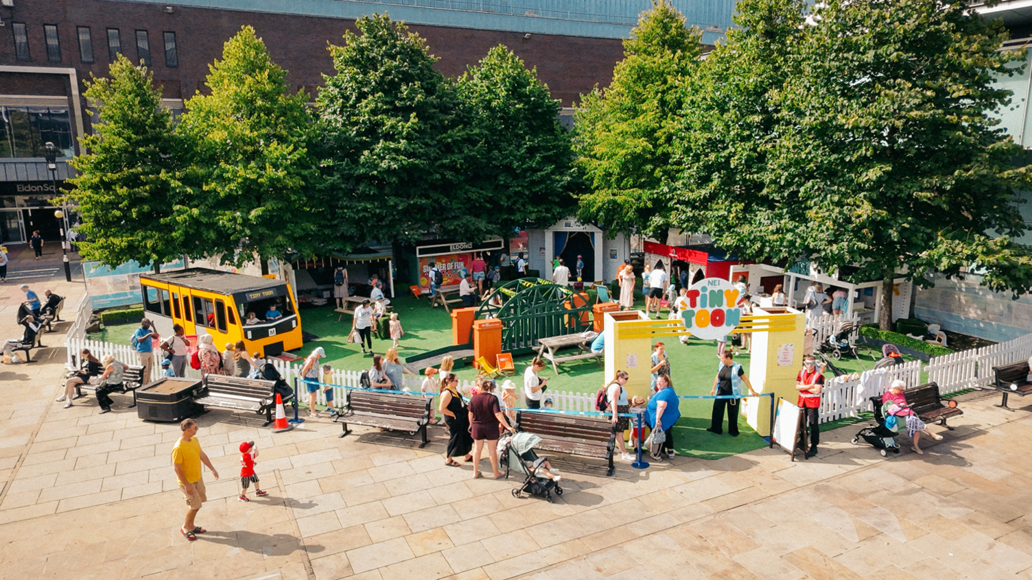A picture looking down at a section of Old Eldon Square in Newcastle. A play area called Tiny Toon has been installed featuring play equipment in the shape of the Tyne Bridge and a yellow Metro train.