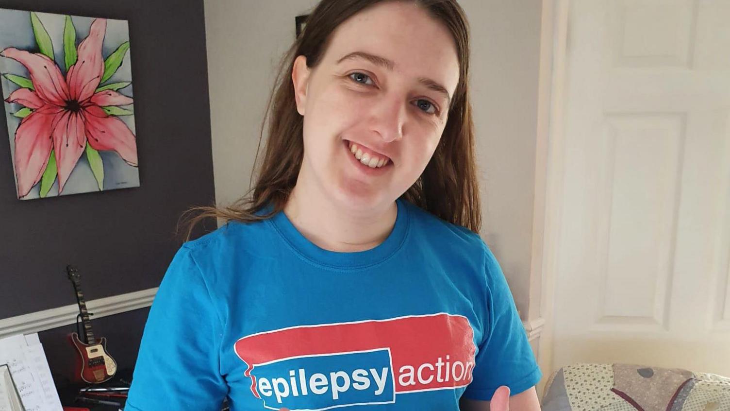 A young woman with dark hair stands smiling in a blue charity t-shirt