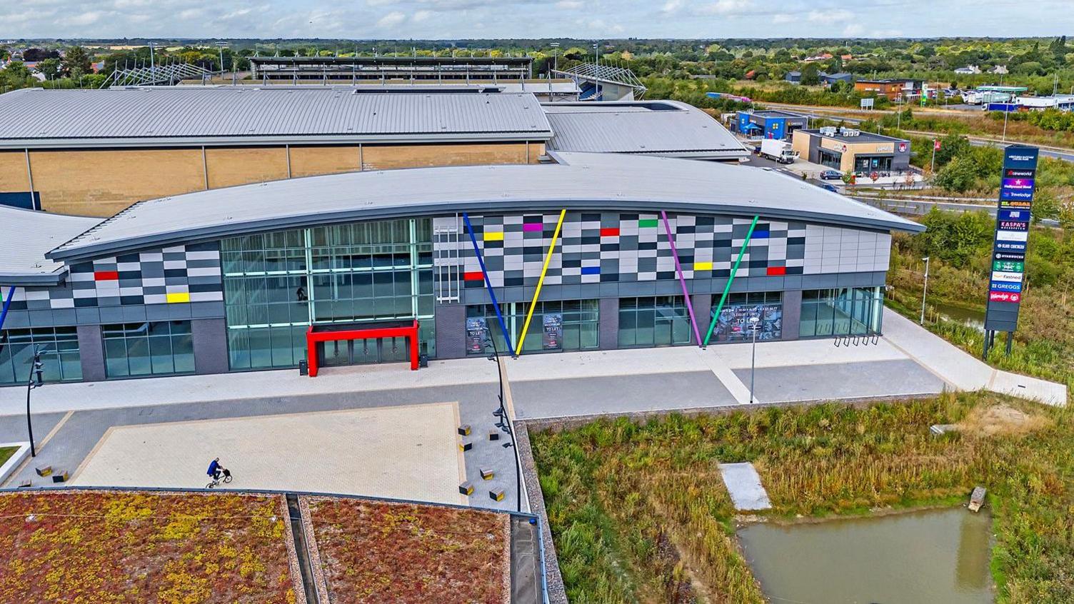 An aerial view of an empty unit at a leisure park. It is a mostly grey building with some coloured blocks and beams.