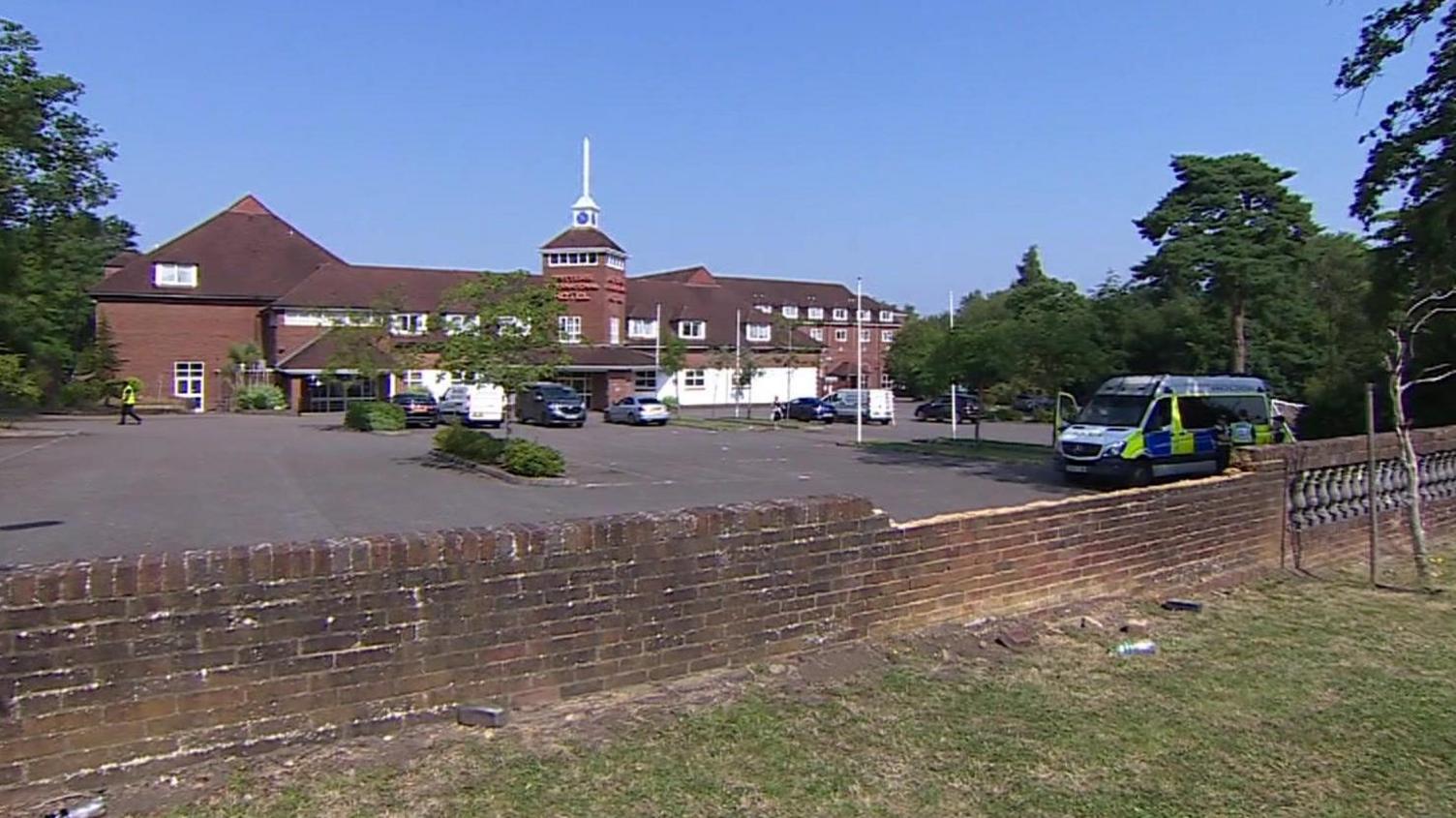 Exterior view of red brick hotel with car park in front. Police van is parked in the car park.