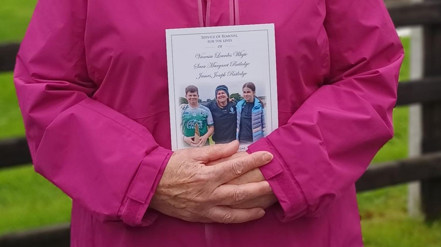 An elderly women wearing a pink coat is holding an order of service. 