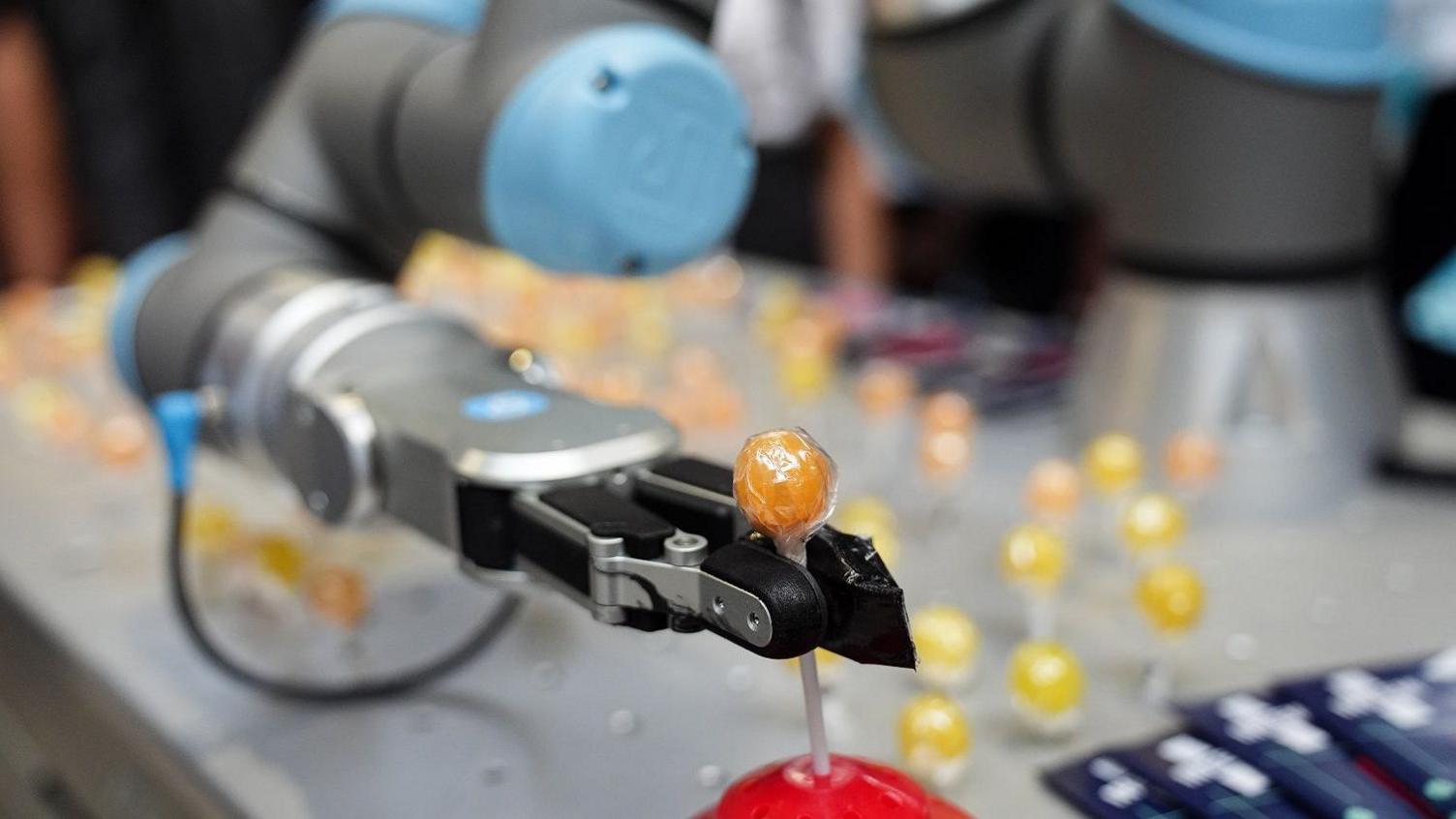A robotic arm is lifting a lollipop out of a holder with metal pincers.