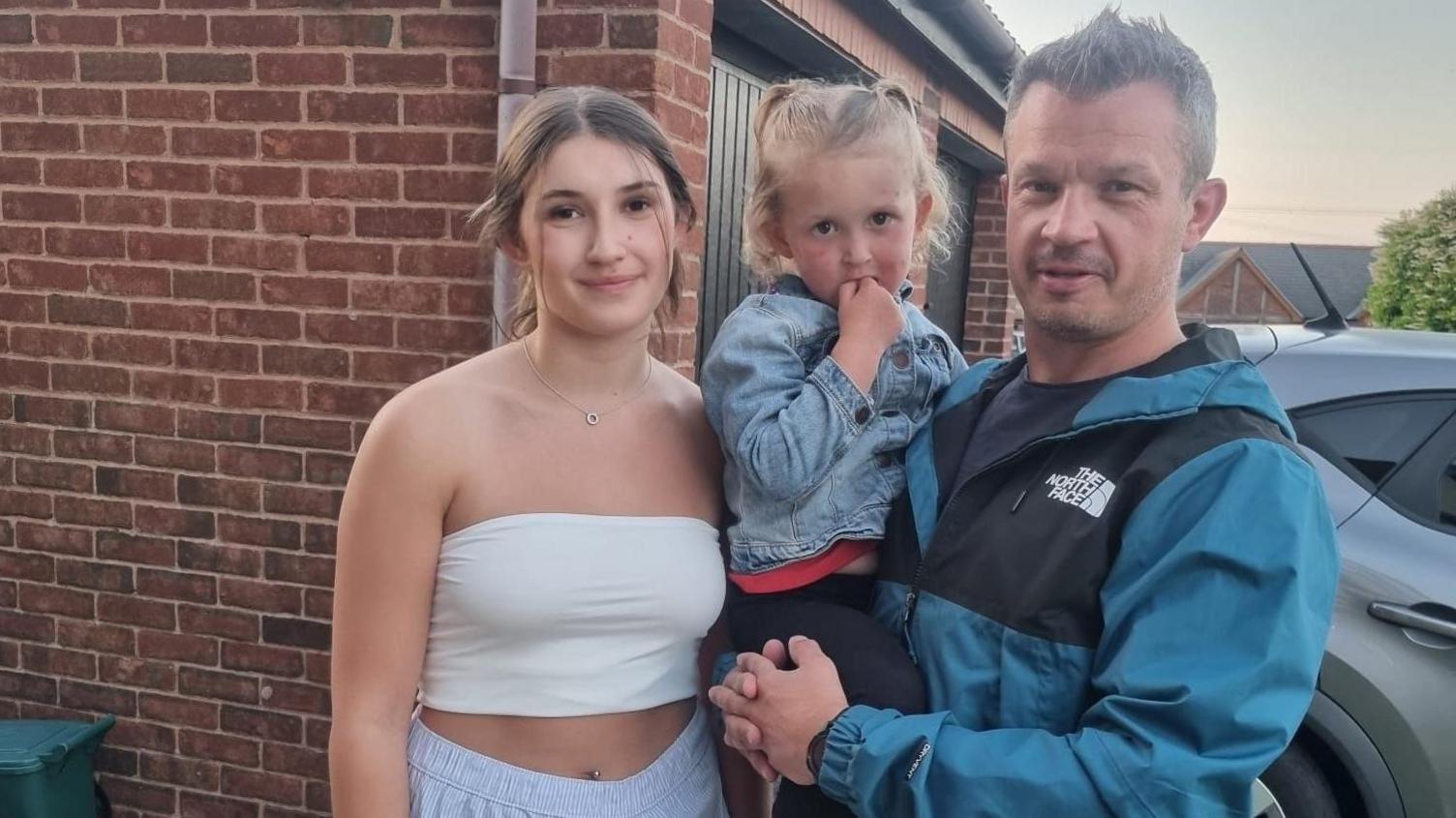 Stuart Phillips stands next to his adult daughter, holding his toddler