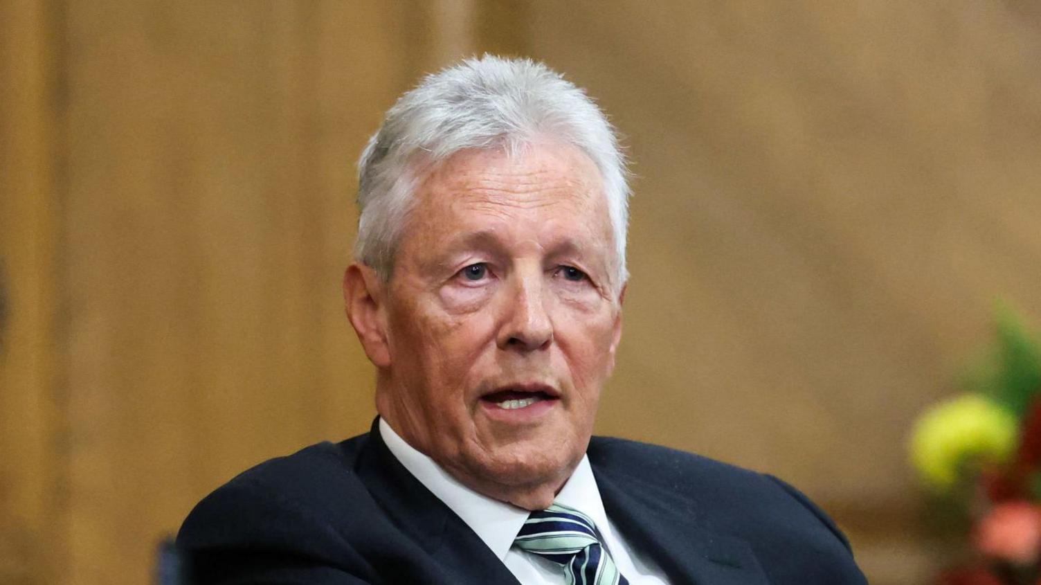 Pater Robinson. He has short white hair, wearing a navy blazer, white shirt and green and navy tie.