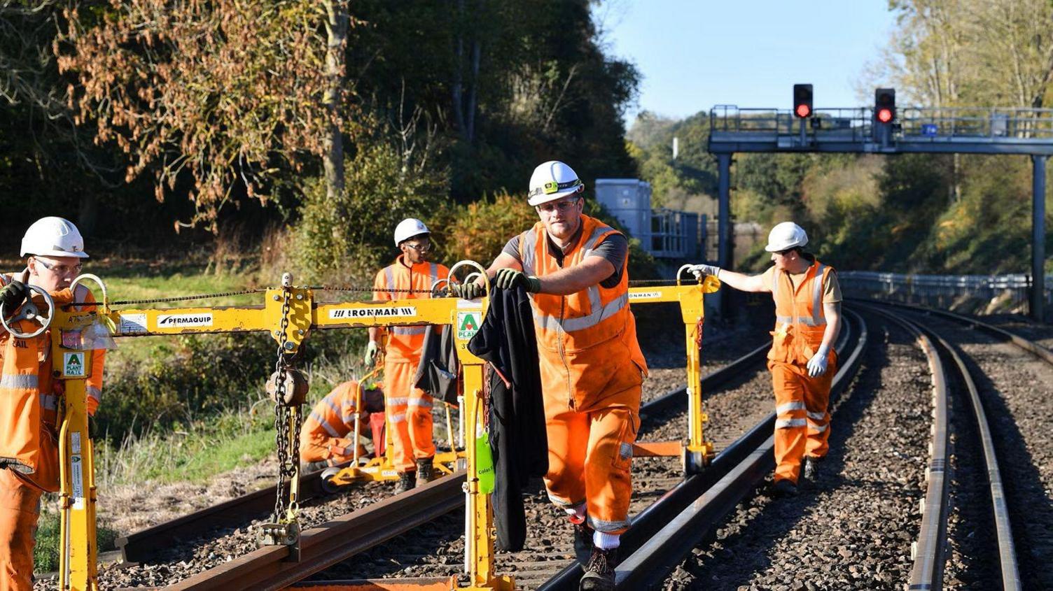 Five contractors wearing orange hi-vis clothing carrying out maintenance work on a railway line.