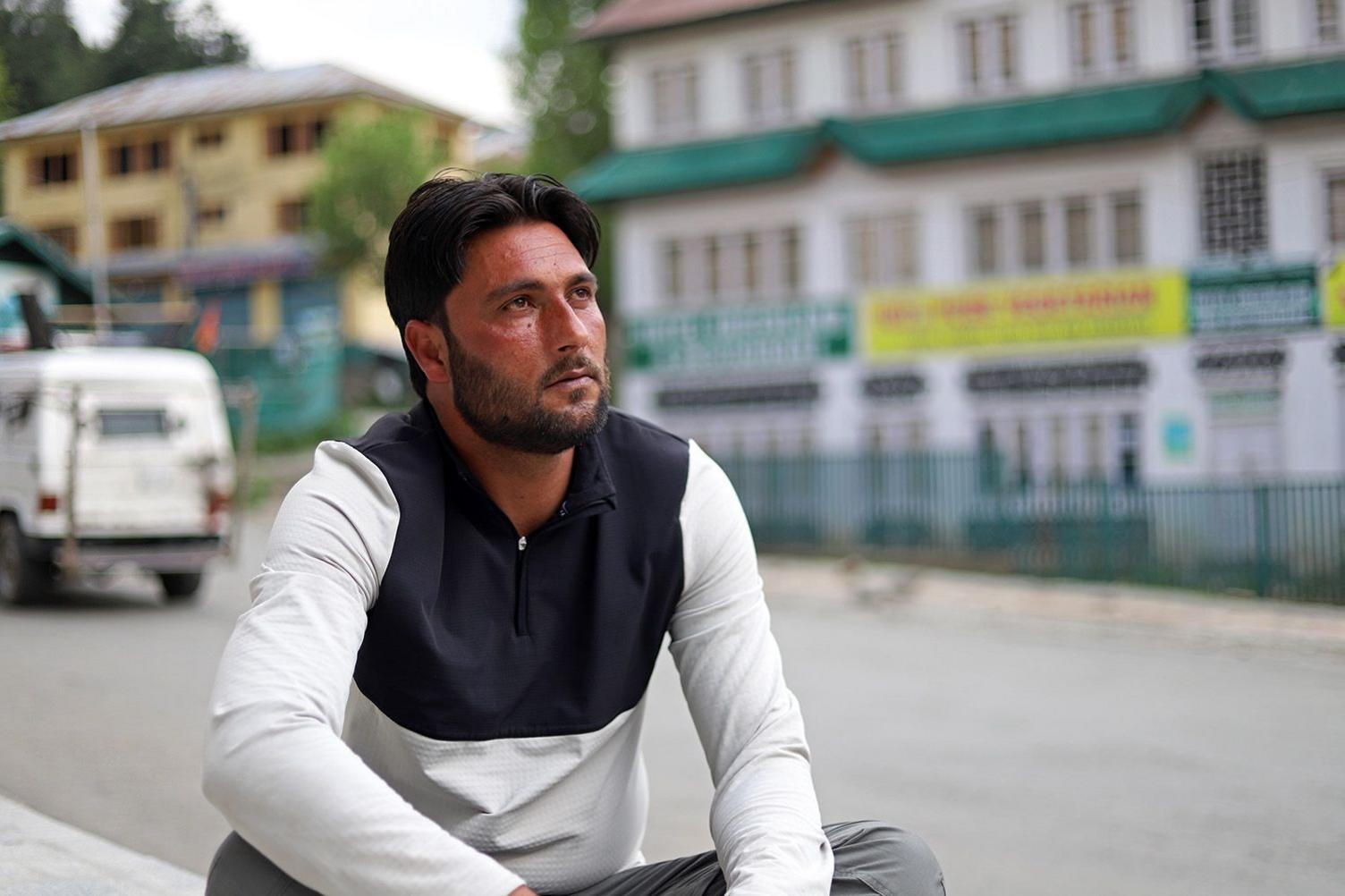 A man sitting on the side of a street with buildings in the background.