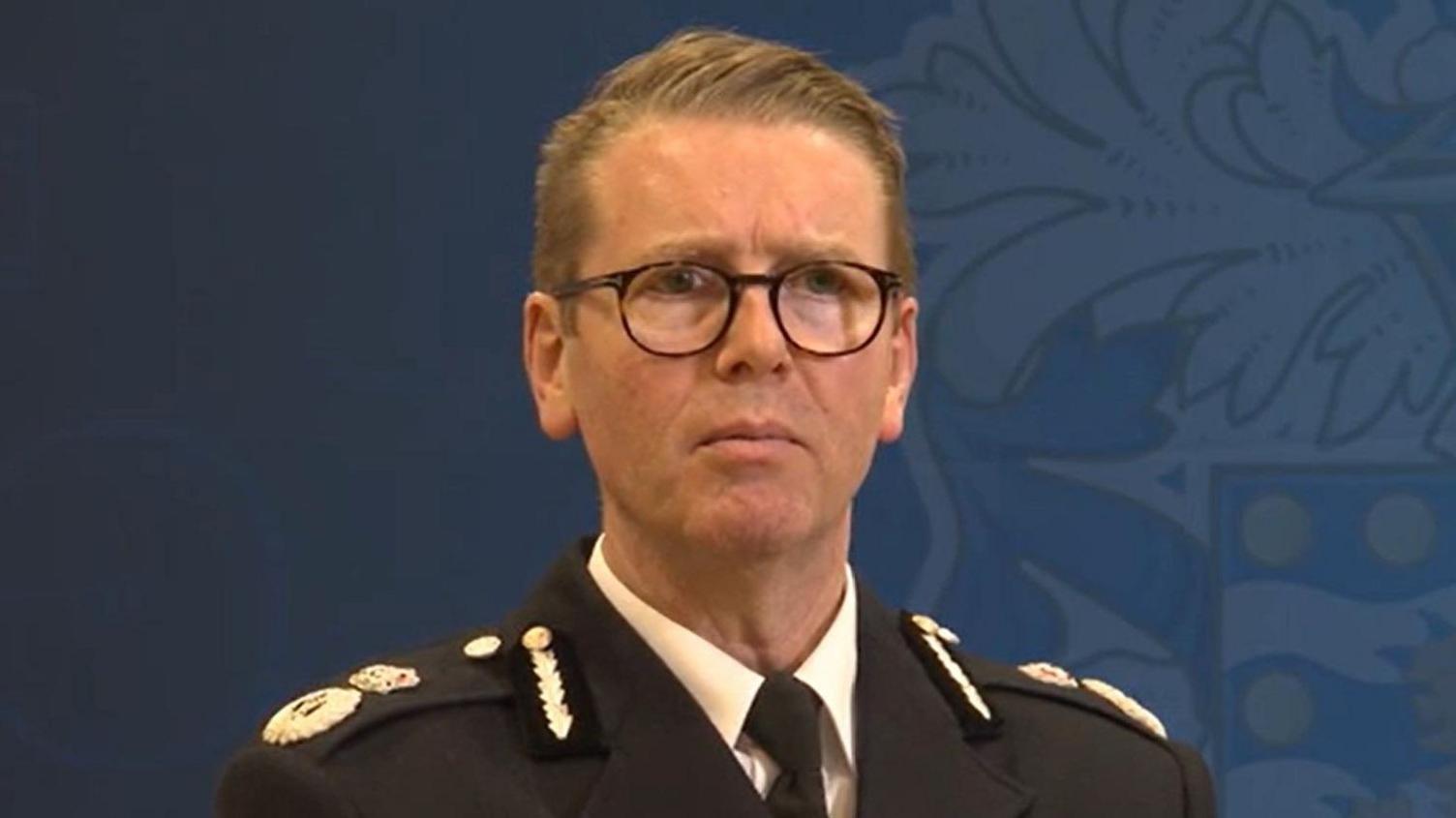 Chief Constable Will Kerr stands in front of a Devon and Cornwall Police sign. He is in full uniform but is not wearing a hat.