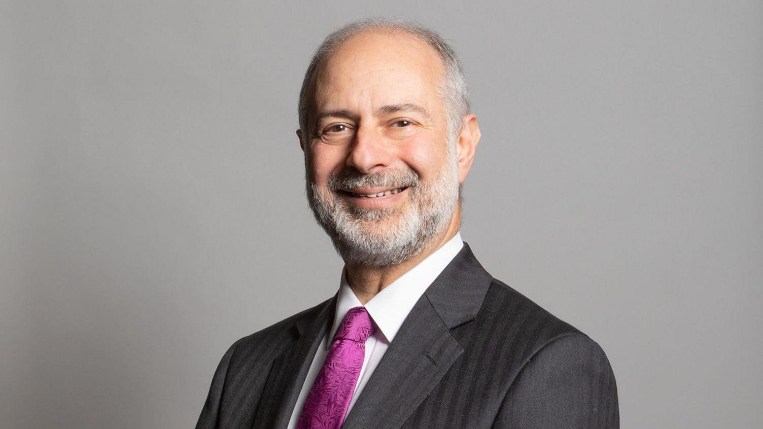 Leeds North East MP, Fabian Hamilton has grey hair and a beard. He wears a suit with a purple tie.
