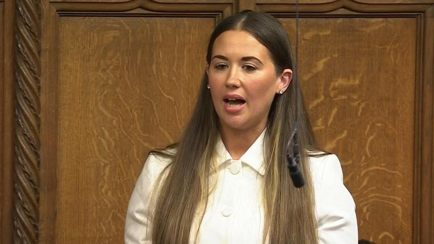 Sorcha Eastwood speaking in the house of commons. She is wearing a white top and holding a piece of paper in front of her.