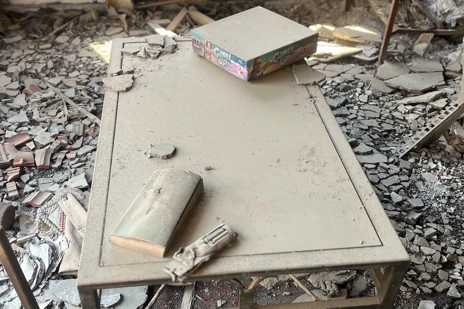 A board game, notebook and burnt remote control remain on a dusty coffee table 