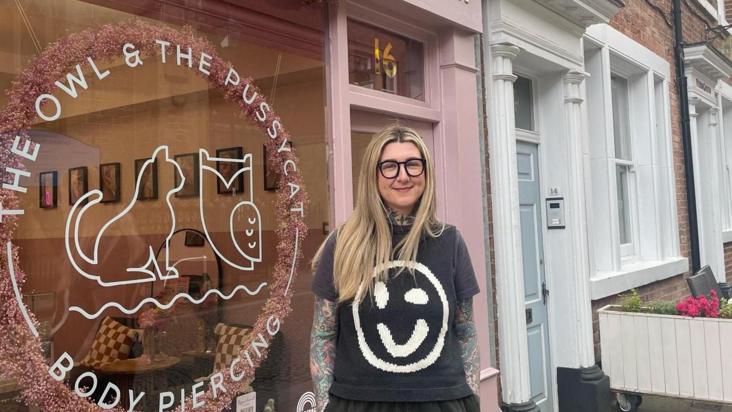 Woman stands in front of a pink shop front