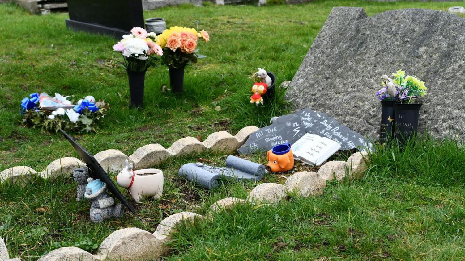 Mass grave for a baby in a Wirral cemetery with artificial flowers and pot animals on it