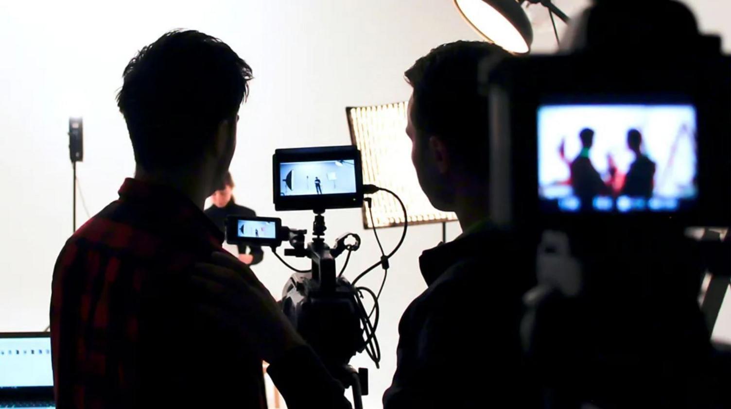 Producers and members of a filming crew gather around a camera on a set. 
