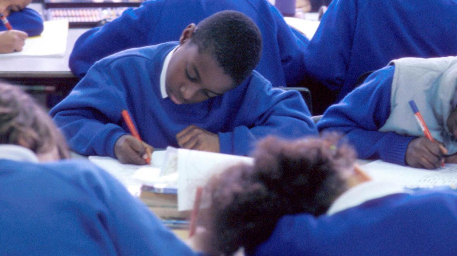 Junior (Primary) school pupils (students/children)in a classroom sitting and writing in their books. Children are of mixed ethnic origin (Black/White).