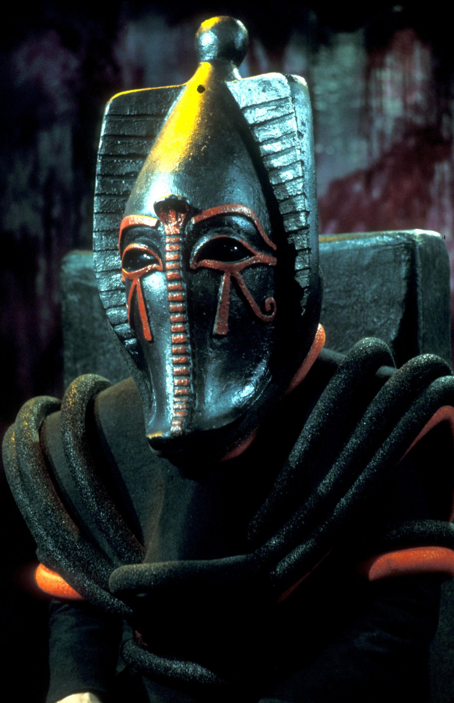 Head and shoulders image of Sutekh, wearing black robes with red trim and an Egyptian styled black mask with red decoration around the eyes