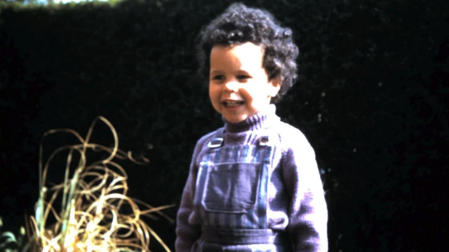 Fielder as a young girl, with short black curly hair and wearing a purple jumper and blue, striped dungarees.