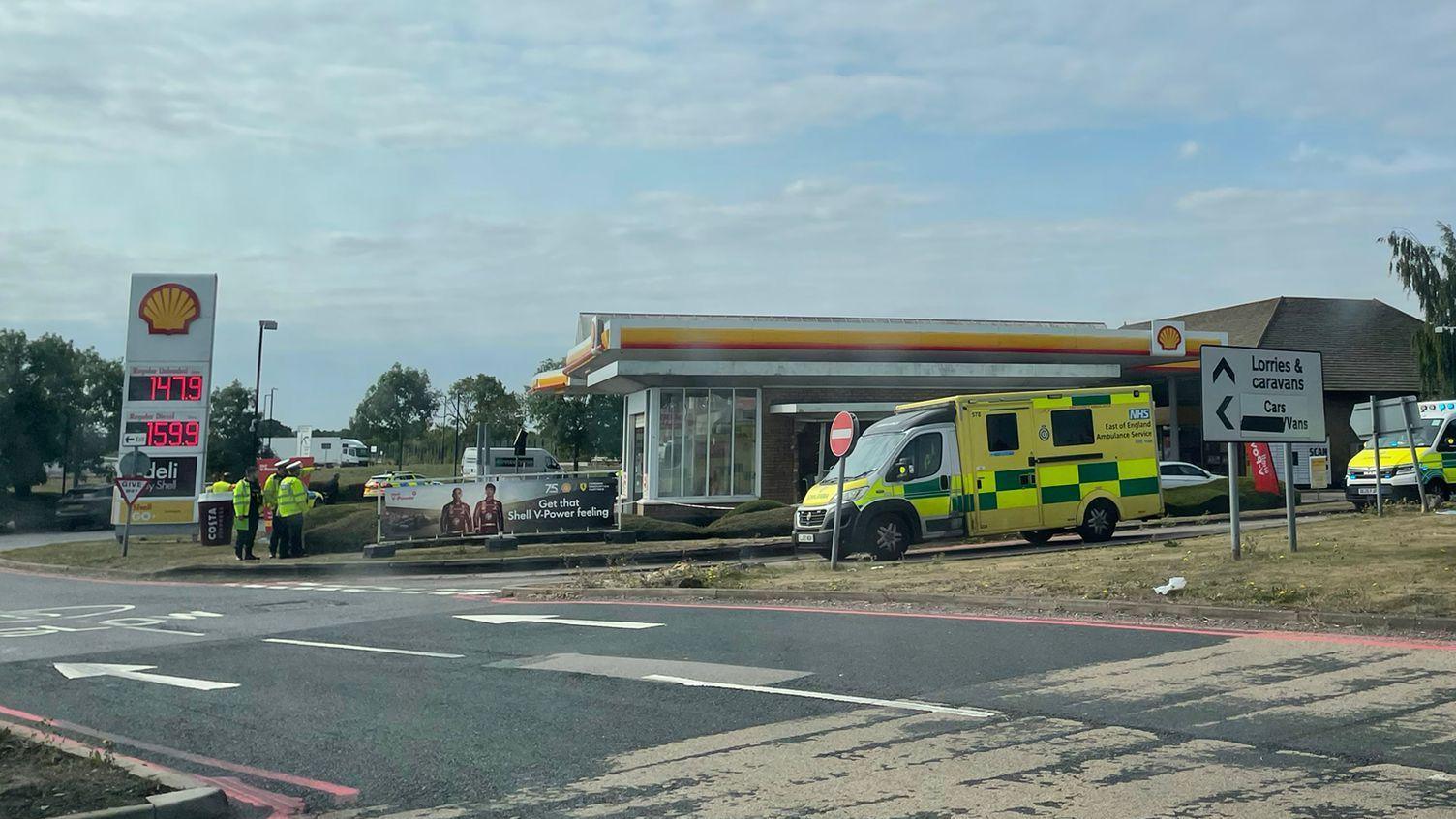 Exterior image of the Shell petrol station with yellow and red signage - with green ambulances parked in front.